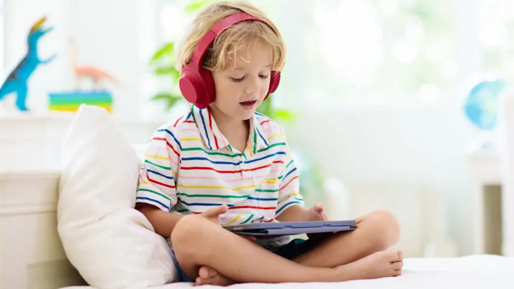 A young boy enjoying a read-along audiobook, he's wearing headphones and this is a picture for an article about the Surprising Benefits of Read-Along Audiobooks in Classrooms and Homeschools