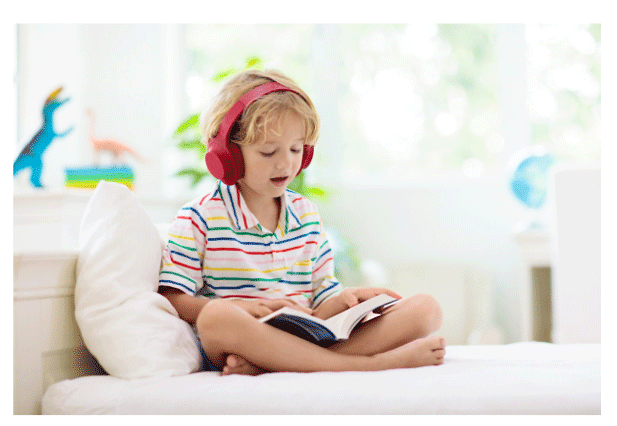 A blond boy reading the fully illustrated, 180-page book of Lost on Infinity, a truly immersive storytelling experience. He wears headphones to listen to the audiobook version while he reads along.